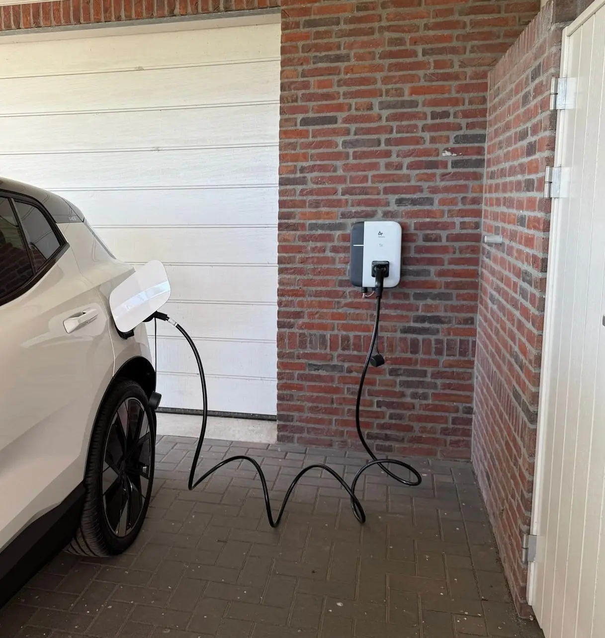 Laadpaal aan de muur van een carport, met een auto aan de laadkabel